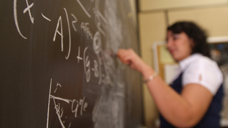 Woman writing equations with a white chalk on a blackboard.